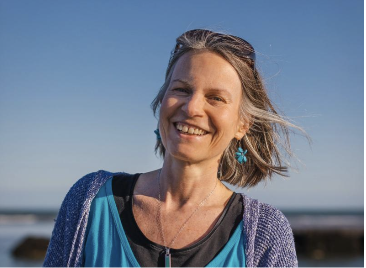 Nicky Torode smiling outdoors, wearing blue earrings