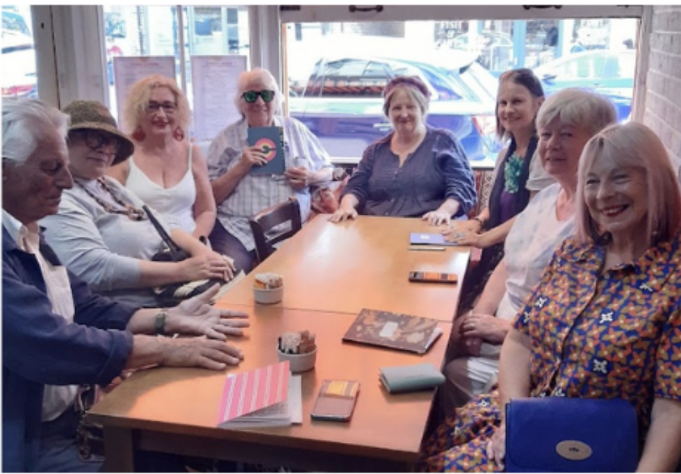 A group of writers around a café table, one holding up a notebook