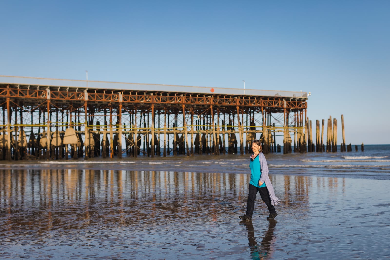 Nicky walking on the wet sand beside Hastings pier under a clear blue sky