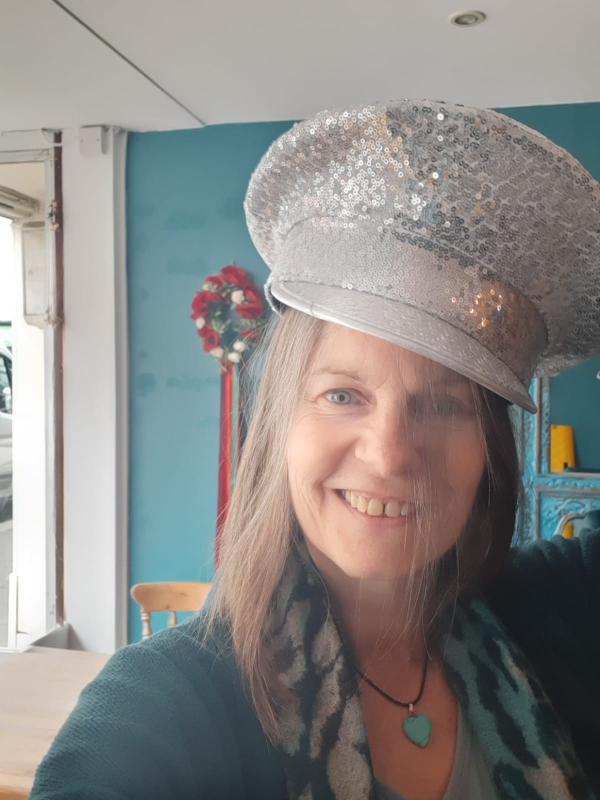 Nicky smiling in a silver sequinned cap in a bright blue cafe