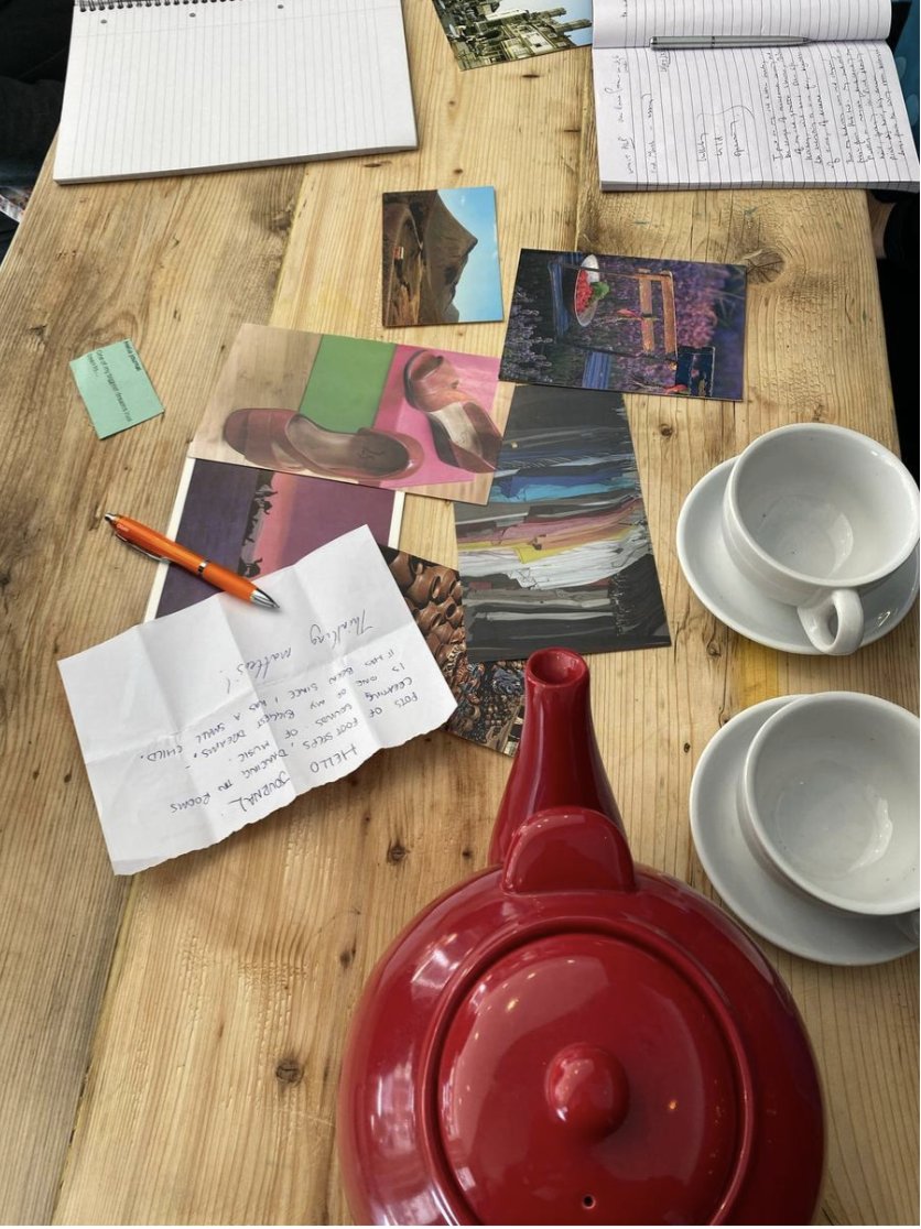 A wooden table with a red teapot, postcards, notebooks and a handwritten note